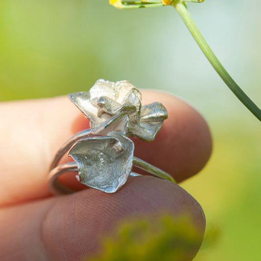 Silver ring with floral design held between fingers against a blurred natural background