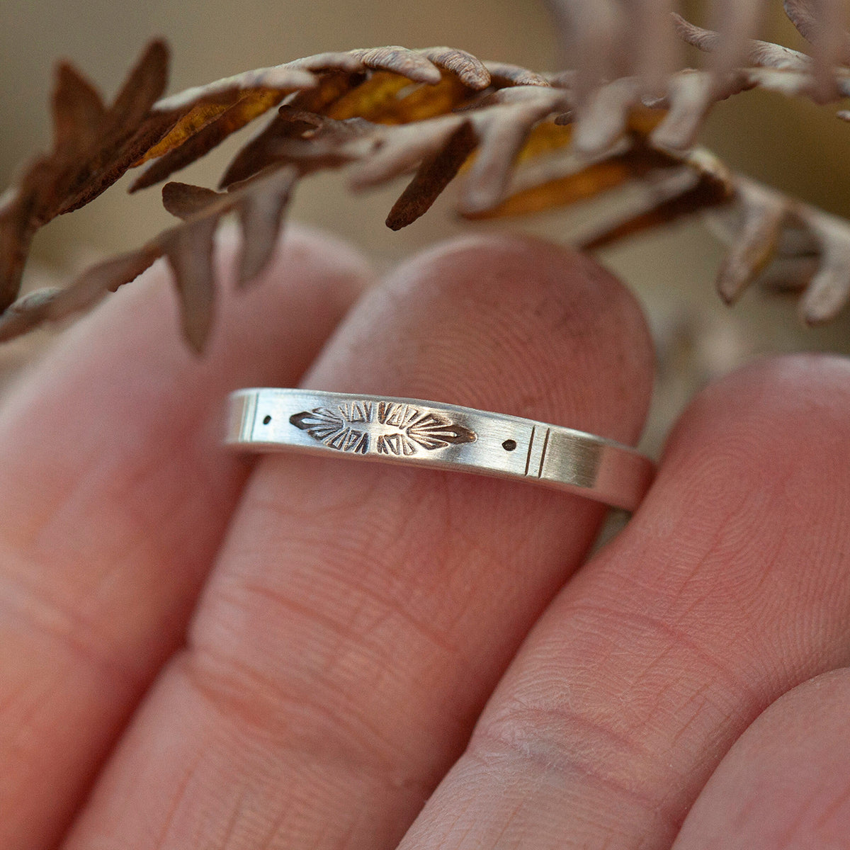 Silver ring with intricate design on a finger, with a blurred natural background