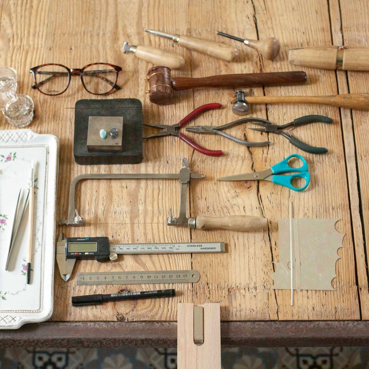 Silversmithing tools laid out on the workshop bench: saw frame, files, pliers, calliper and sketchbook