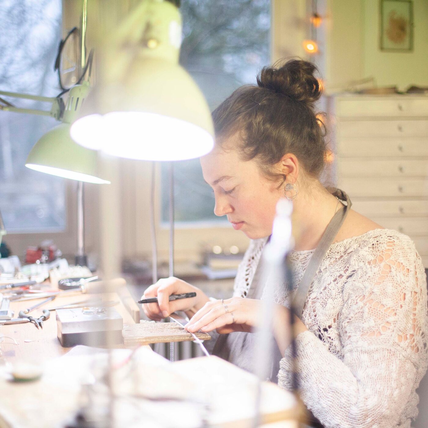 Ushas working on a silver piece at her bench, under the lamp of her workshop